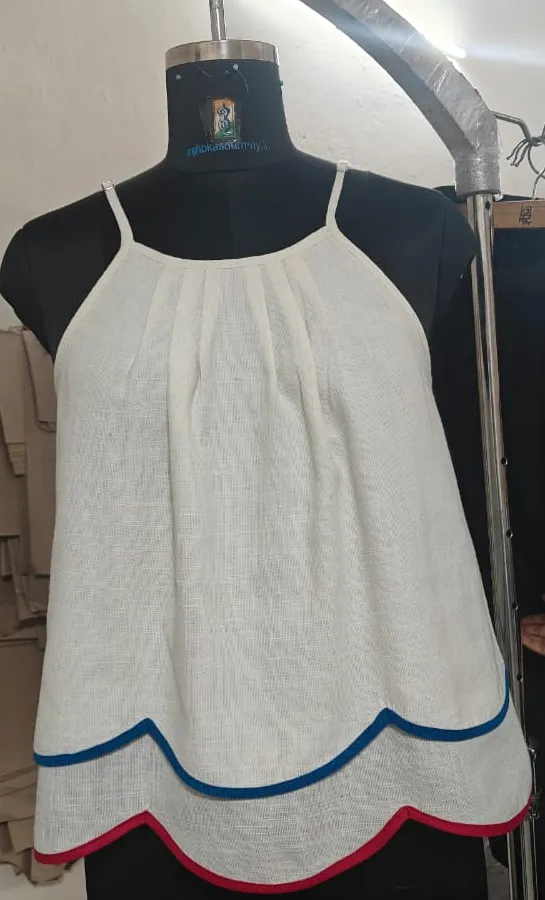White linen halter top with pleats and scalloped hem with blue and red piping on a dress form